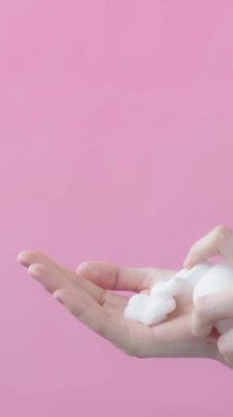 İzole edilmiş pembe arka planda el köpüğü sabunu ya da köpük yüz temizleme yüz bakımı hijyen sağlığı parmak presi kullanan şişeden köpük alan genç bir kadın.