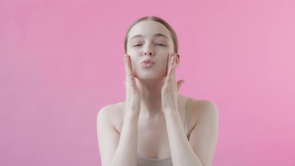 ピンクのバックグラウンドに完璧な肌を持つかなり若い女性は 笑顔をポーズし 空気のキスを送信します 化粧品スキンケア製品を使用した快楽のコンセプト ピンク バックグラウンド ビューティーコレクション — ストック動画