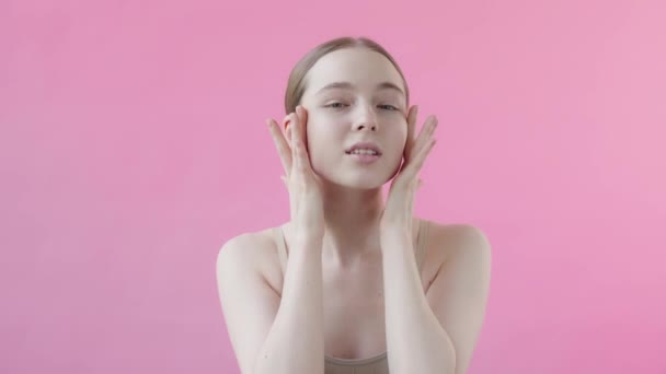 20多岁的年轻女士把血清涂在脸上 看着相机 粉色背景 迷人的专业模型与完美的清洁皮肤使用面部美容产品 护肤广告的概念 — 图库视频影像