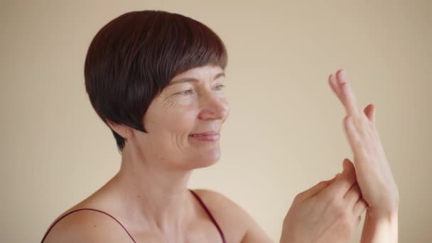 白种人50多岁的成熟女人在皮肤上涂上乳膏 然后按摩分发 可爱的女性 呵护美丽 手感柔软流畅 化妆品 — 图库视频影像