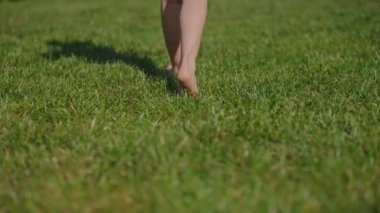 Küçük bir çocuk çıplak ayakla yürüyor, çimlerin üzerinde gölge gibi. Çok yavaş çekimde, küçük kızın küçük ayakları parkta yürüyordu. Mutlu aile kavramı, çocukluk, rüya, hayat, hareket.
