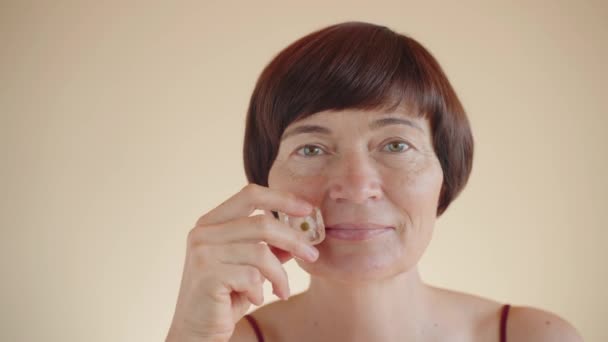 护肤中年妇女用冰块触摸着脸 冰块里有一个洋甘菊 有机纯素化妆品的概念 延缓老化过程 舒缓或镇静霜 — 图库视频影像