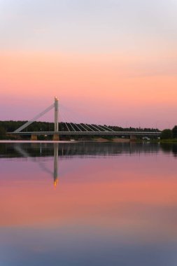 Dikey fotoğraf. Rovaniemi Finlandiya 'da güzel bir gün batımı. Kutup günü. Laponya 'ya gidiyorum. Köprünün üstünde pembe gökyüzü. Kuzeyde bir tatil. Sudaki yansıma. Renk farkı. Fantastik İskandinavya