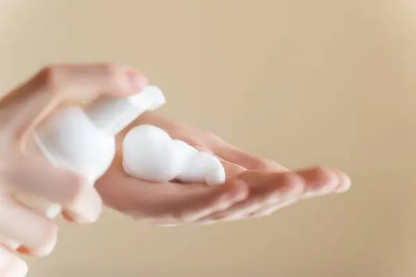 Extreme close up, palm of hands on isolated background, young woman applying hand foam soap or foam to wash face, skin care, cleansing, hygiene, health care. Finger presses taking foam from bottle