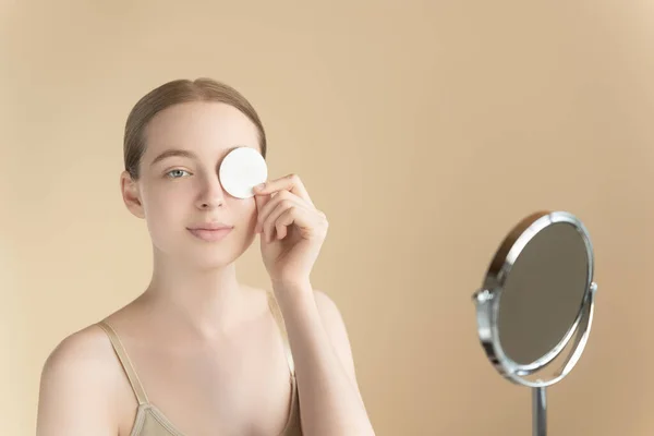 stock image Caucasian attractive young woman 20s on a beige background with perfect skin holding a cotton pad in one hand. Skin care, makeup removal, toner or micellar water application, cleansing, beauty routine