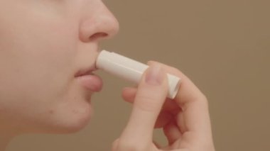 Dudak kremi süren ve nemlendirici etkisi olan aşırı yakın plan genç bir kadın. Stüdyo çekimi, bej arka plan, fotokopi alanı, dudak kremi reklamcılığı konsepti.