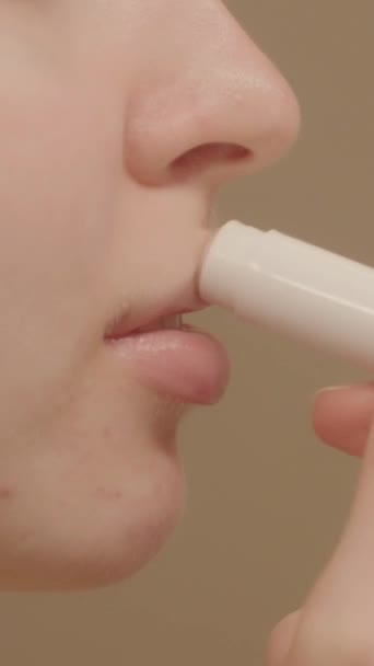 非常密切的年轻女性使用唇膏和享受一个很好的保湿效果 工作室拍摄 米色背景 唇膏广告概念 社交网络的垂直视频 — 图库视频影像