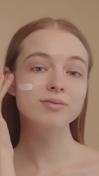 年轻的女士看着相机 用一个手指放香料面霜 广告防晒霜化妆品 面部处理及保护一位年轻女子的肖像日常美容美发12个垂直视频 — 图库视频影像