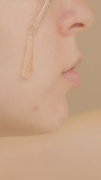 白种人年轻女性的面部特写照片将护肤血清放在面颊上的米色背景 护肤血清广告 复制空间 垂直录像 — 图库视频影像