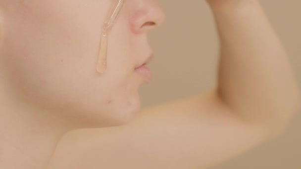 白种人年轻女性的面部特写照片将护肤血清放在面颊上的米色背景 护肤血清广告 复制空间 — 图库视频影像
