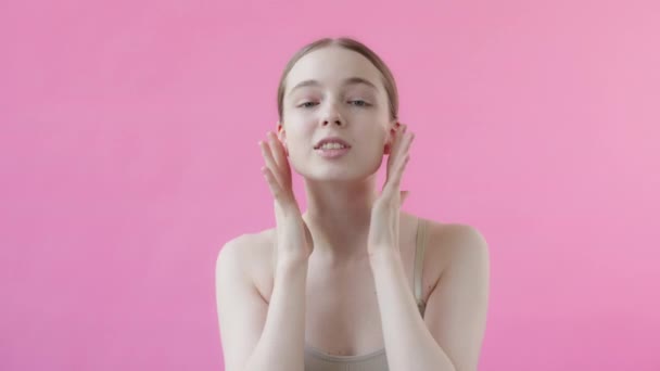 年轻健康的金发女子20多岁时面带微笑地抚摸着光滑的皮肤 粉红背景工作室拍摄的护肤概念 — 图库视频影像