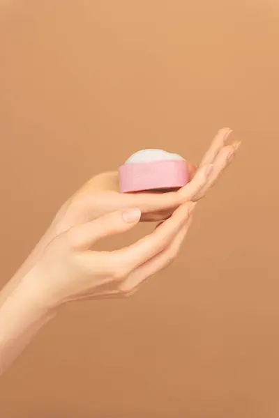 Close-up of female hands palm with pink solid face cleanser or hand foamy soap on isolated peach background. skin care advertising copy space. Vertical photo
