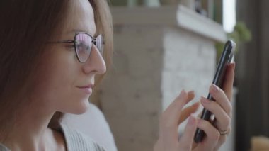Rahatlamış genç bir kadın haberlere bakmak ve evdeyken mesaj göndermek için telefonunu kullanıyor. Yeni sosyal medyaya abone oluyor, internetten alışveriş yapıyor, internetten sipariş veriyor. Milenyum kadınları mobil cihazlarla vakit geçirir..