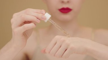 Cilt bakım serumlu damlatıcıyı tutan güzel bir kadının kadın ellerine yakın çekim. Yavaş çekimde, kadın izole edilmiş bej arka plana serum damlatıyor. Güzellik ürünleri reklamları, cilt bakım serumu.