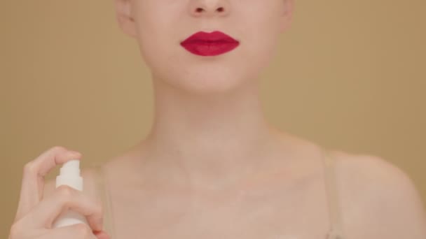 慢动作美丽的白种女人 用润肤的身体喷雾 涂在她天然健康的颈部皮肤上 米色孤立的背景 女性无法辨认的肖像化妆品广告 — 图库视频影像