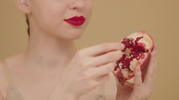 極端なクローズアップ女性の赤い唇とチンテイスティングザクロの種 アンチエイジング製品 スキンケア広告 健康的な食事 ベージュの背景にスタジオで隔離された減量ダイエットを示す女性 スローモーション — ストック動画