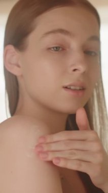 Ağır çekim. Çıplak tenli, genç, zayıf, sarışın bir kız parmaklarıyla omzuna dokunuyor ve aynanın önünde vücudunu çeviriyor. Kadın vücut losyonu sürüyor ve cilde masaj yapıyor. Vücut bakım reklamları