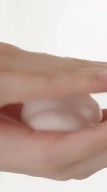 Dikey video. Yakın plan, genç kadın elleri, sabun köpüğü, yüz köpüğü, bebek sabunu, vücut hijyeni. Vücut bakım ürünleri reklam konsepti, cilt bakımı. Yavaş çekim.