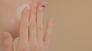 Güneş kremi süren bir kadın, sabah güzellik tedavisi. Tanınmayan beyaz bir kadın krem sürüyor. Sağ eliyle. Bej arka planda makyaj malzemesi var. Deri bakımı konsepti. Kozmetik reklamı