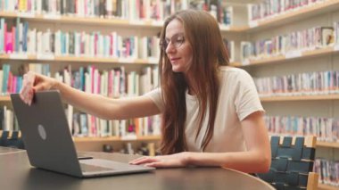 Bilgisayarlı beyaz bir bayan üniversite öğrencisi kütüphanede uzaktan kumandalı bir internet semineri izliyor, internetten canlı yayın yapıyor ya da bir kampüste sanal toplantı düzenliyor, bir iş projesi üzerinde çalışıyor..