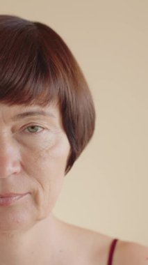 Güzel, beyaz, 50 'li yaşlarda, dikey, yarı yüz portresi. Reklam, cilt bakımını gençleştiriyor ve sağlıklı cilt için makyaj yapıyor. Kişisel bakım. Dikey video. Yavaş çekim.