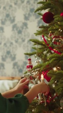 Dikey video. Yakından bakan yeşil elbiseli kız, Noel ağacını süslüyor ren geyiği oyuncağı taşıyor, Mutlu Yıllar arifesi. Mutlu Noeller sinematik video koleksiyonu. 