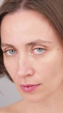 Dikey ekran: Moda modeli stüdyoda. Beyaz tenli genç kadının çarpıcı yüzü kameraya güvenle bakıyor. Esmer, mutlu kadın portresi. Yakın çekim. Doğal makyaj malzemesi reklamları.