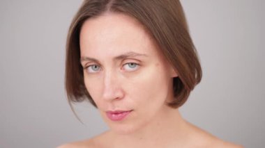 Stüdyoda manken. Beyaz kadının çarpıcı yüzü kameraya kendinden emin bir şekilde bakıyor. Esmer estetik kadın, güzellik portresi, yakın plan, doğal makyaj. Gri arka plan. Cilt bakımı. Kozmetik reklamları