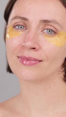 Dikey video: Göz bandı reklam konsepti. Yüzünde göz altı iyileşme bantları olan estetik bir kadın. Çekici, sakin esmer kadın stüdyoda kameraya bakıyor. Cilt Kozmetik Dermatoloji Yenilenme Kaplıcası
