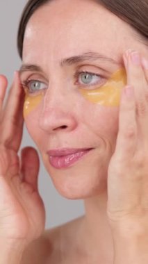 Dikey video: Göz bandı reklam konsepti. Estetik kadın göz altı iyileşme bantları uyguluyor. Stüdyodaki çekici, sakin esmer kadın. Kozmetik Güzelliği Rutin Dermatoloji Gençleştirme Spa Cilt Bakımı