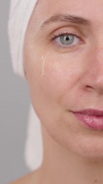 Dikey video: Yüzünde pipeti olan güzel bir kadın yüz serumu uyguluyor. Yüz bakımı için estetik prosedürler. Makyaj hazırlığı. Yarım yüz portresi.