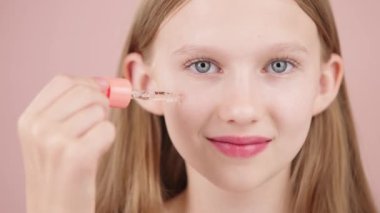 Gülen bir kızın portresi. Yüzüne serumu damlatan bir kızın portresi. Pembe arka planda mavi gözlü sarışın beyaz kız. Gençler için reklam konsepti cilt bakımı.