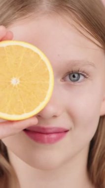 Çok yönlü bir video. Komik sarışın bir kızın canlı bir portresi. Elinde turuncu bir göz, stüdyoda kameraya bakıyor. Doğal kozmetik ürünleri, vitaminler, sağlıklı beslenme ve alışkanlıklar, güzellik ve gençlik.