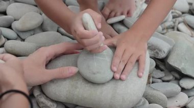 Anne ve çocukların ellerinin plaj kayasında taşlarla tic-tac-toe oynamaları yaz aylarında basit, çevre dostu açık hava oyunlarıyla bağ kurma eğilimini yansıtıyor..