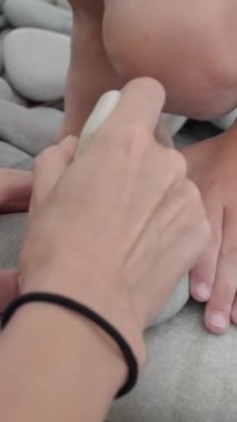 Dikey video: Anne ve çocukların ellerinin bir plaj kayasında taşlarla tic-tac-toe oynadığı bir yakın çekim, yaz aylarında basit, çevre dostu açık hava oyunlarıyla bağ kurma eğilimini yansıtıyor.