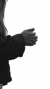 Dikey video: Tanınmayan bir kadın, yardım için ellerini kenetlemiş, beyaz arka planda duruyor. İnancın dingin atmosferi ve ruhsal bağlantı, ibadet ve övgü, umut. Siyah ve beyaz