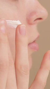 Genç bir kız ve yanağında da bir tutam krem var. Yüzüne nemlendirici krem ya da güneş kremi süren bir kadının yakın çekimi. Sabah cildi rutini. Kozmetik ürün reklamcılığı.