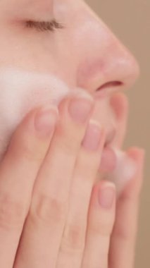 Yüzüne nazikçe temizleyici köpük süren bir kadının yakın çekimi, sağlıklı, ışıl ışıl bir cilt ve doğal güzelliğini arttıran günlük cilt bakımını yapıyor..