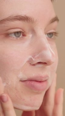 Genç ve güzel bir kadın nazikçe temizleyici köpük sürüyor, yüzünü yıkıyor ve sağlıklı cilt için günlük cilt bakımını yapıyor. Günlük güzellik hizmetleri için reklam kavramı.