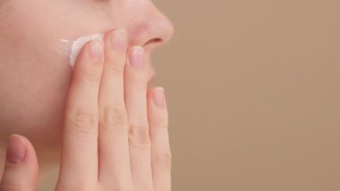 Bir kadının yakın plan çekimi nemlendirici, yüz kremi ya da güneş kremini yanaklarına sürer. Stüdyoya vakıf makyajı yapan genç bir kız. Sabah cildi rutini. Kozmetik ürünler için konsept reklamlar. Boşluğu kopyala