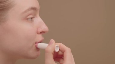 Dudak kremi süren, dudaklarını yumuşacık, pürüzsüz ve sağlıklı bir görünüş için besleyen, nemlendiren, güzellik ve kendine bakım rutinini geliştiren güzel bir genç kadının yakın plan profili.