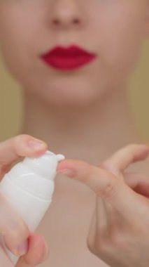 Genç bir kadının beyaz bir şişeden yüz kremi sürerken ve makyaja hazırlanırken yakın plan görüntüsü. Cilt bakımı, makyaj hazırlığı, güzellik rutini ve kişisel bakım. Bulanık arkaplan.
