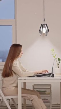 Modern bir dairede dizüstü bilgisayarla yazı yazan genç bir kız öğrenci. Sınavlara hazırlanmak, yeni bir proje üzerinde çalışmak, yapay zeka araçlarını kullanarak sunum yapmak, araştırma yapmak, kendini geliştirmek. Dikey Video