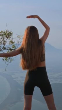 Dikey çekim. Tanımlanamayan kadın. Spor kıyafetleri giyen genç atletik dişiler sırt egzersizleri yapıyor, deniz veya kıyı şeridini nefes kesen manzaranın tadını çıkarıyorlar. Omurga sağlığı. Güzel duruş 