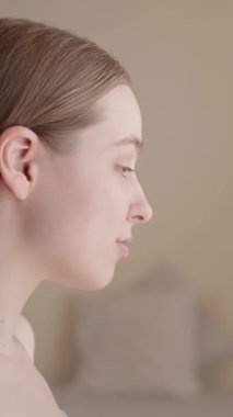 VERTICAL VIDEO Genç kadın aynanın karşısında oturuyor, gülümsüyor ve cilt rutininin sonucuna hayran. Doğal görünüş, sağlıklı parlayan ten, gevşemiş ve tatmin olmuş ifade. Güzellik konsepti