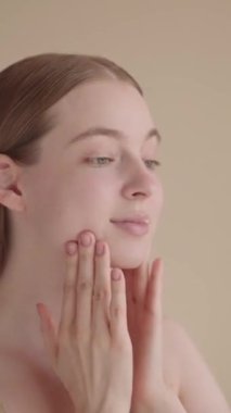 Genç bir kadın cildine dokunarak cilt bakımının sonucuna gülümser ve hayran kalır. Doğal bir görünüş, sağlıklı parlayan bir ten, rahat ve tatmin edici bir ifade. Güzellik ve özgüven..