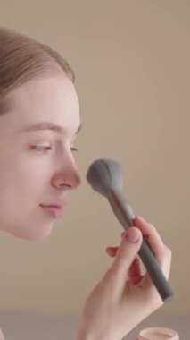 Neşeli genç bir kadın sabah güzellik rutininin bir parçası olarak fırçayla makyaj yapıyor. Mutlu bir Z Geni dişisi kendine bakmaktan ve güne hazırlanmaktan zevk alıyor. Doğal ışıklandırma