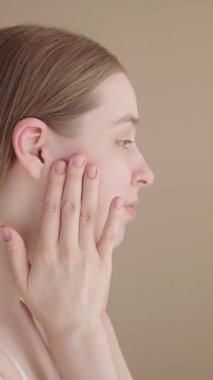 Genç bir kadın gülümsüyor ve cilt rutininin sonucuna hayran, kameraya bakıyor. Doğal görünüş, sağlıklı parlayan ten, gevşemiş, tatmin olmuş ifade. Güzellik ve kişisel bakım konsepti.