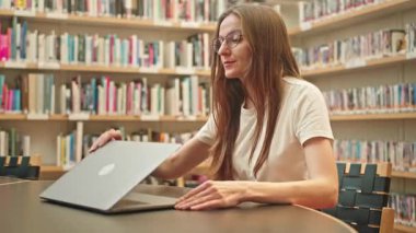 Öğrenci bir üniversite kütüphanesi masasında dizüstü bilgisayar açıyor, araştırmaya başlıyor, sınav hazırlığı, online ders veya kurs, eğitim platformunda bağlantı kuruyor, bir iş projesi üzerinde çalışıyor. Harmanlanmış öğrenme.