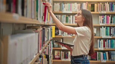 Modern bir üniversite kütüphanesinde elinde tablet olan bir kız öğrenci. Akademik araştırma, modern eğitim, kendi kendini yönetme, yüksek öğrenim, sınav hazırlığı. Harmanlanmış öğrenme. 